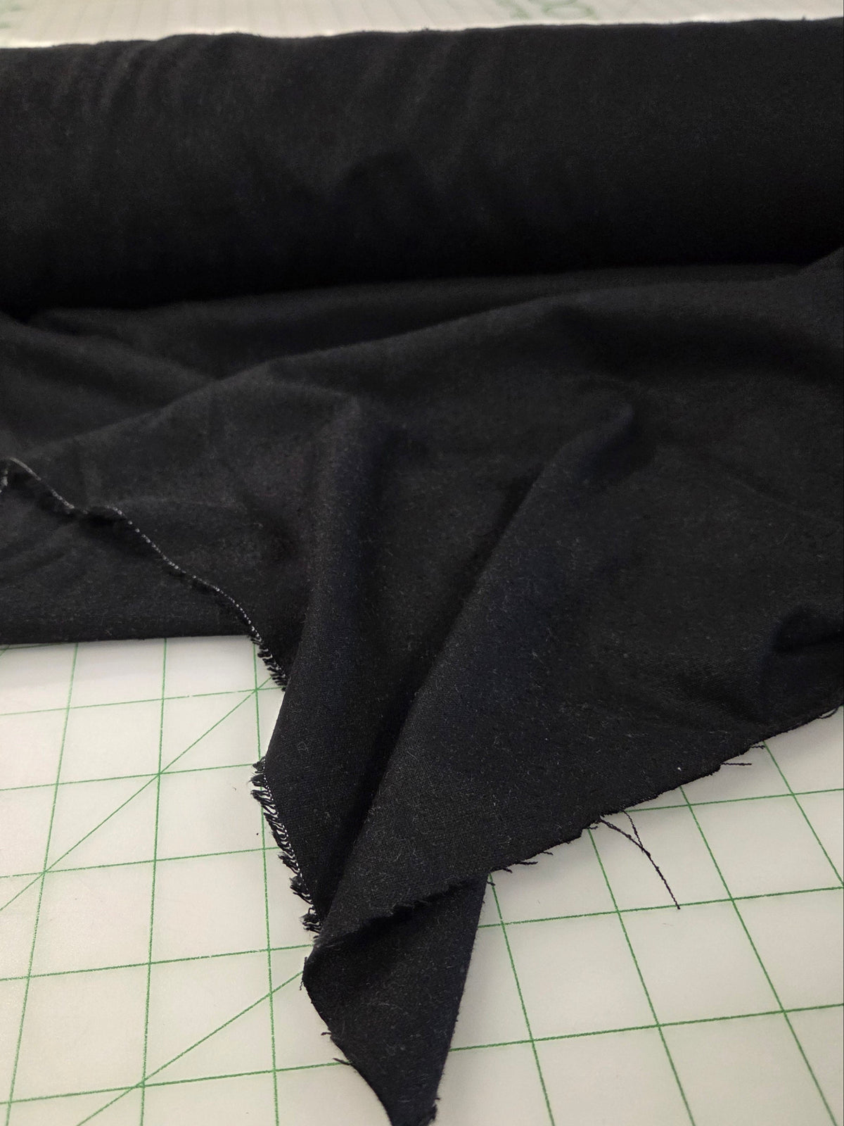 A roll of black fabric partially unrolled on a white cutting mat with green grid lines. black silk noil