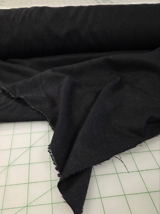 A roll of black fabric partially unrolled on a white cutting mat with green grid lines. black silk noil