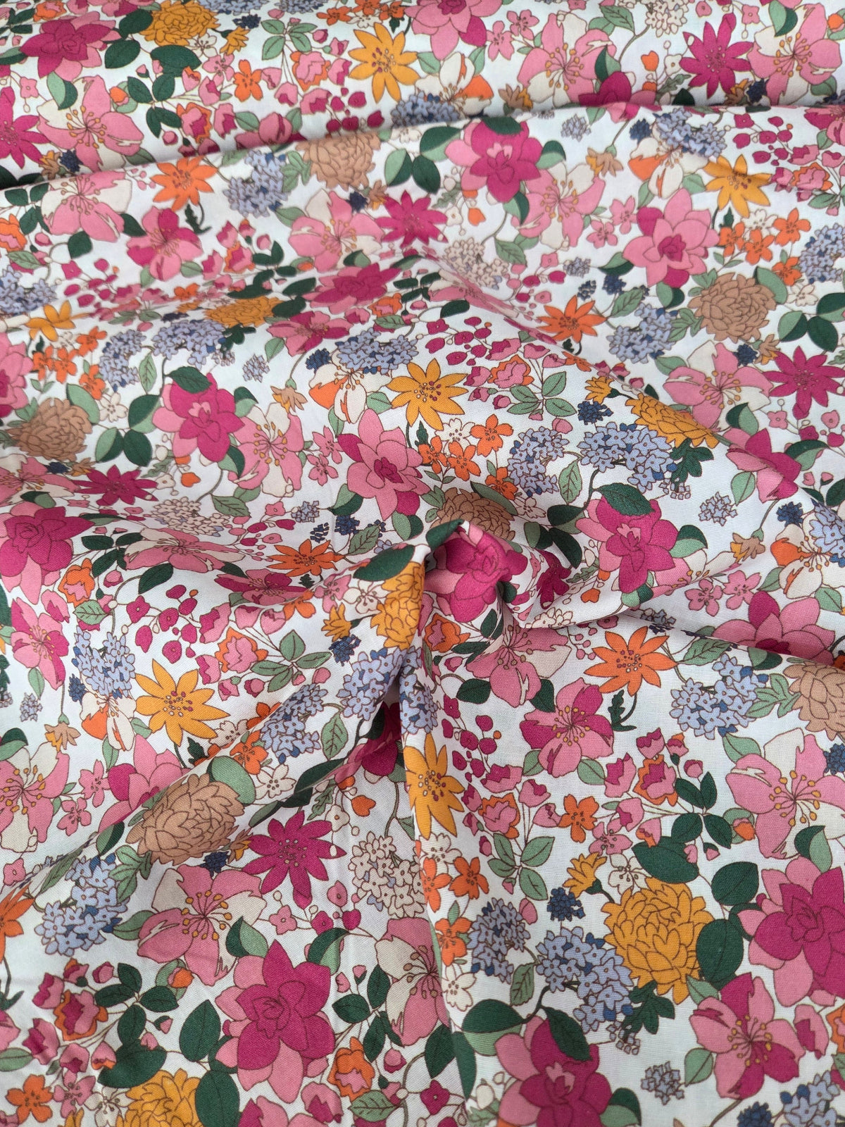 A close-up of a floral fabric with a dense multicolor print featuring pink, orange, yellow, purple, and green flowers on a white background.