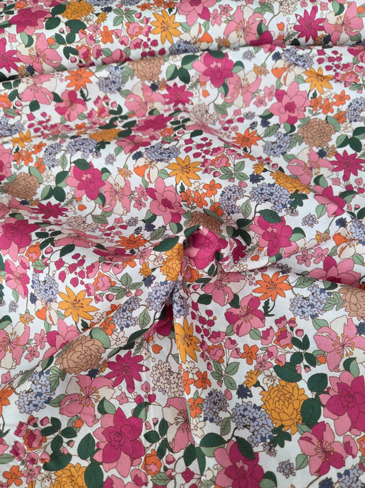 A close-up of a floral fabric with a dense multicolor print featuring pink, orange, yellow, purple, and green flowers on a white background.
