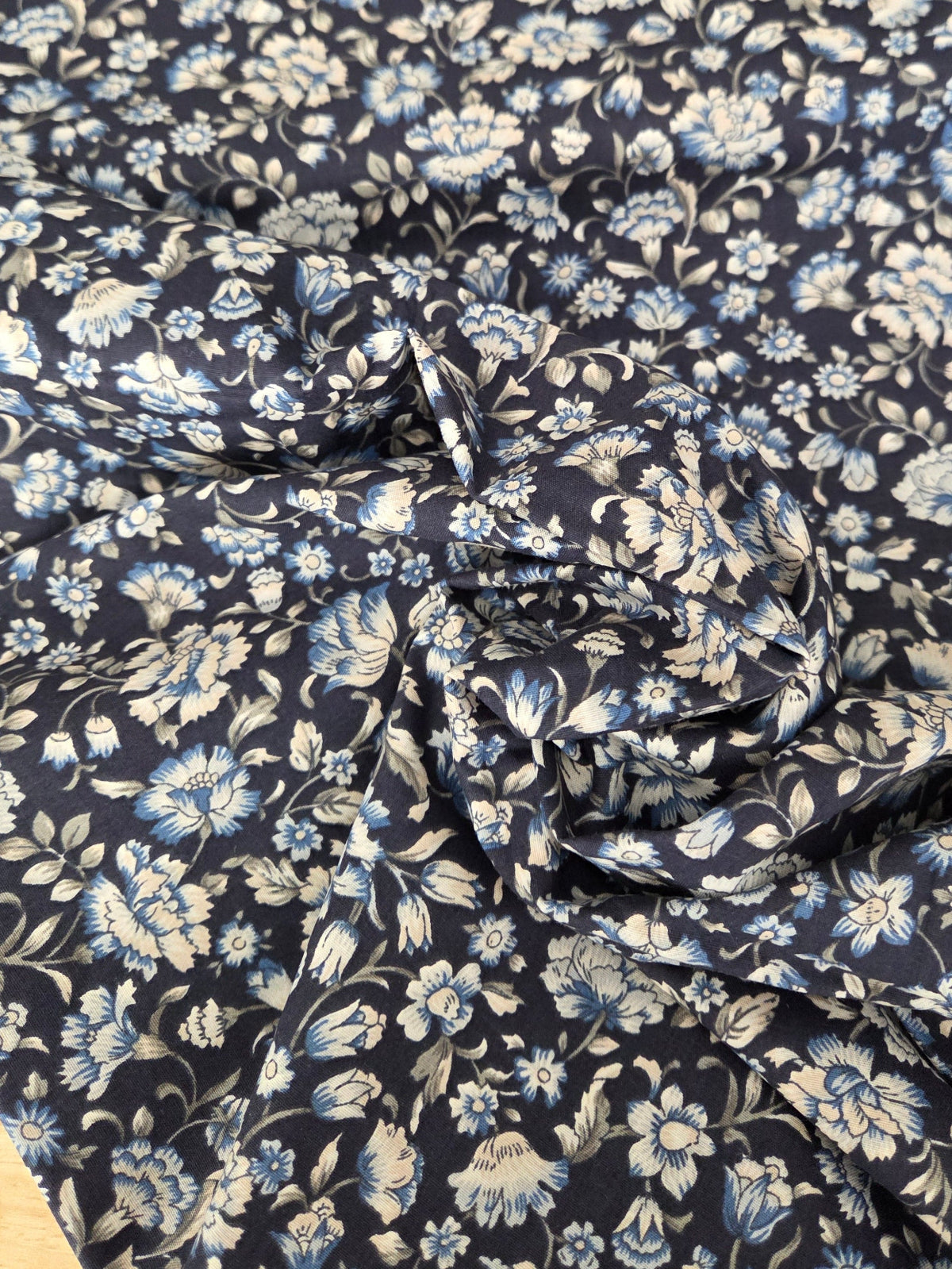 A close-up of a draped fabric with a dense floral pattern in light blue and off-white on a dark navy background.