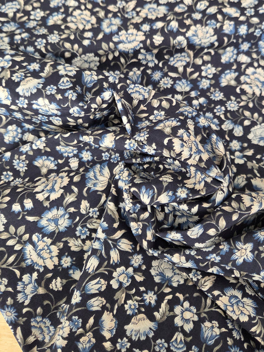 A close-up of a draped fabric with a dense floral pattern in light blue and off-white on a dark navy background.