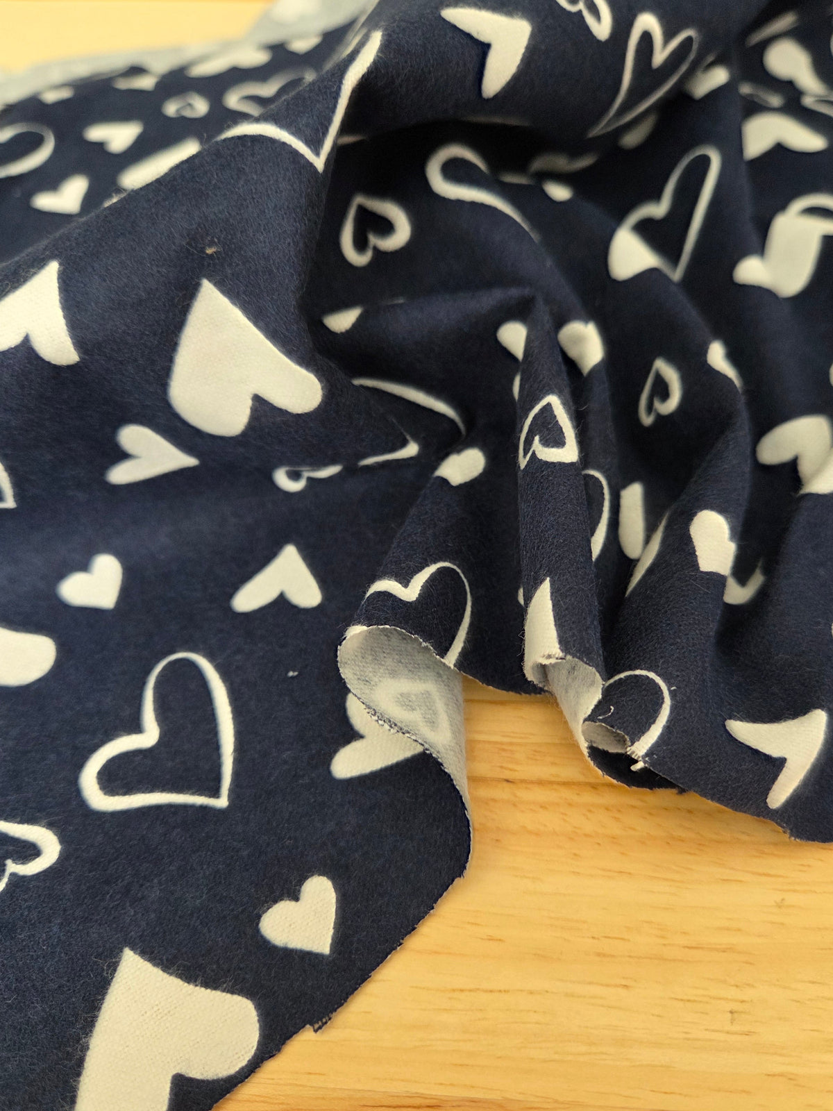 A close-up of navy blue fabric with a white heart pattern, draped over a light wood surface. LA Finch Fabrics