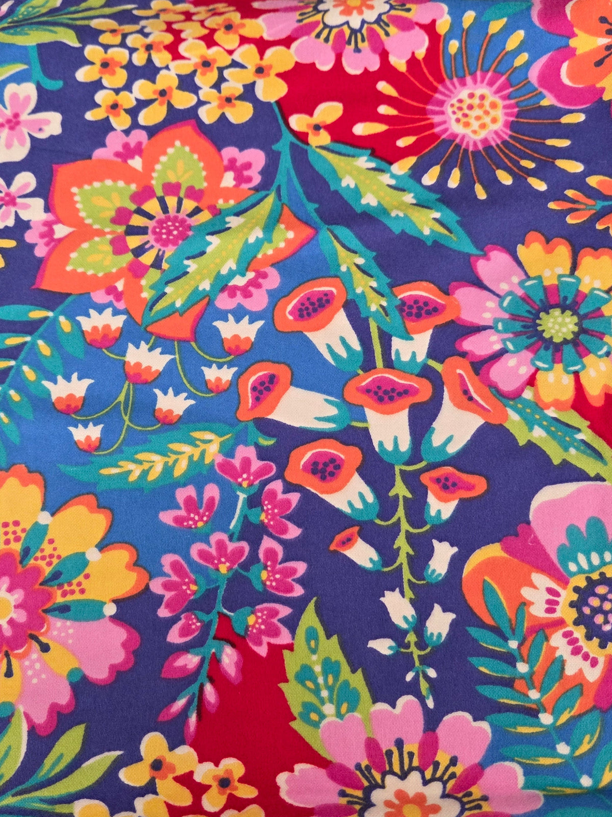 A close-up of a vibrant floral fabric with a dense pattern of multicolored flowers and green leaves on a dark blue background.