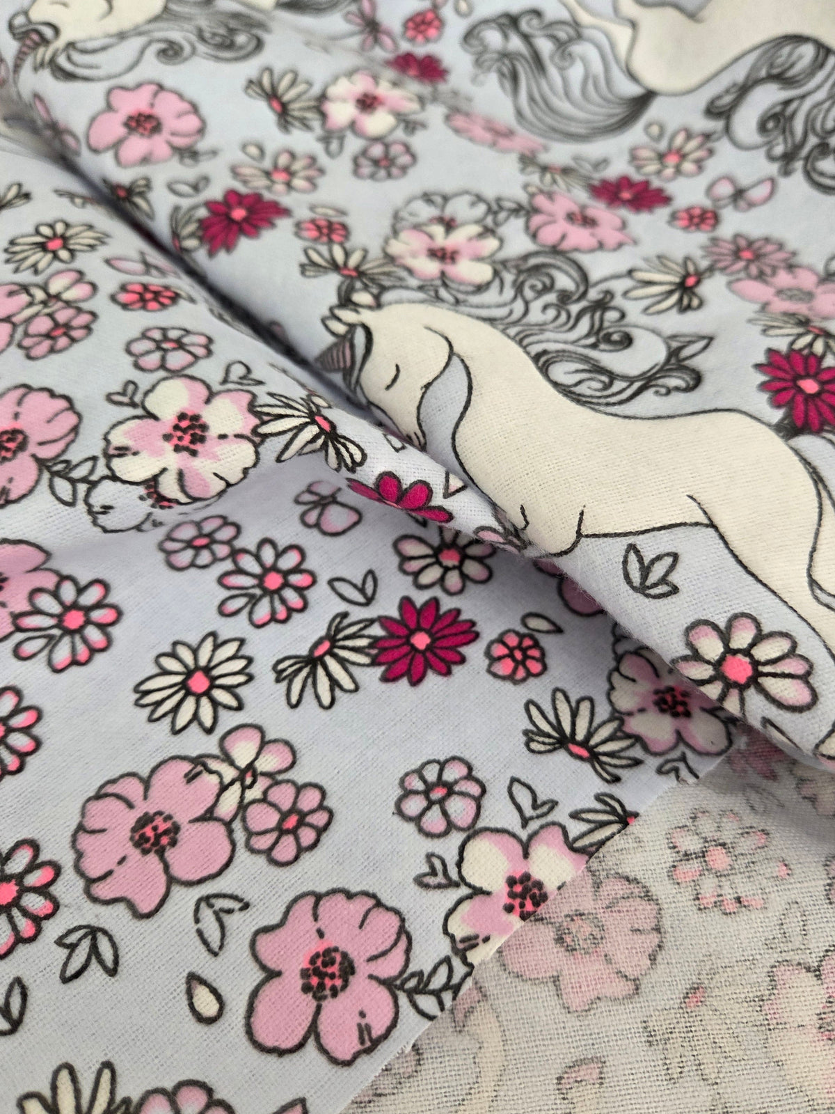 A close-up of patterned fabric with a white horse and pink, magenta, and black floral print on a pale blue-gray background.