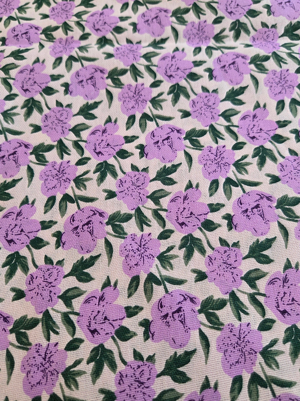 A close-up of a fabric or wallpaper pattern featuring purple flowers and green leaves on a warm beige background.