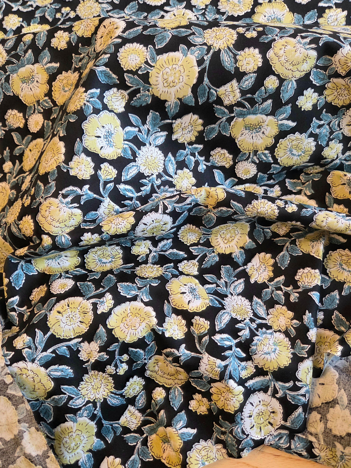 Black brocade fabric with a dense floral pattern in yellow, gold, and light blue, draped to show its texture and sheen.