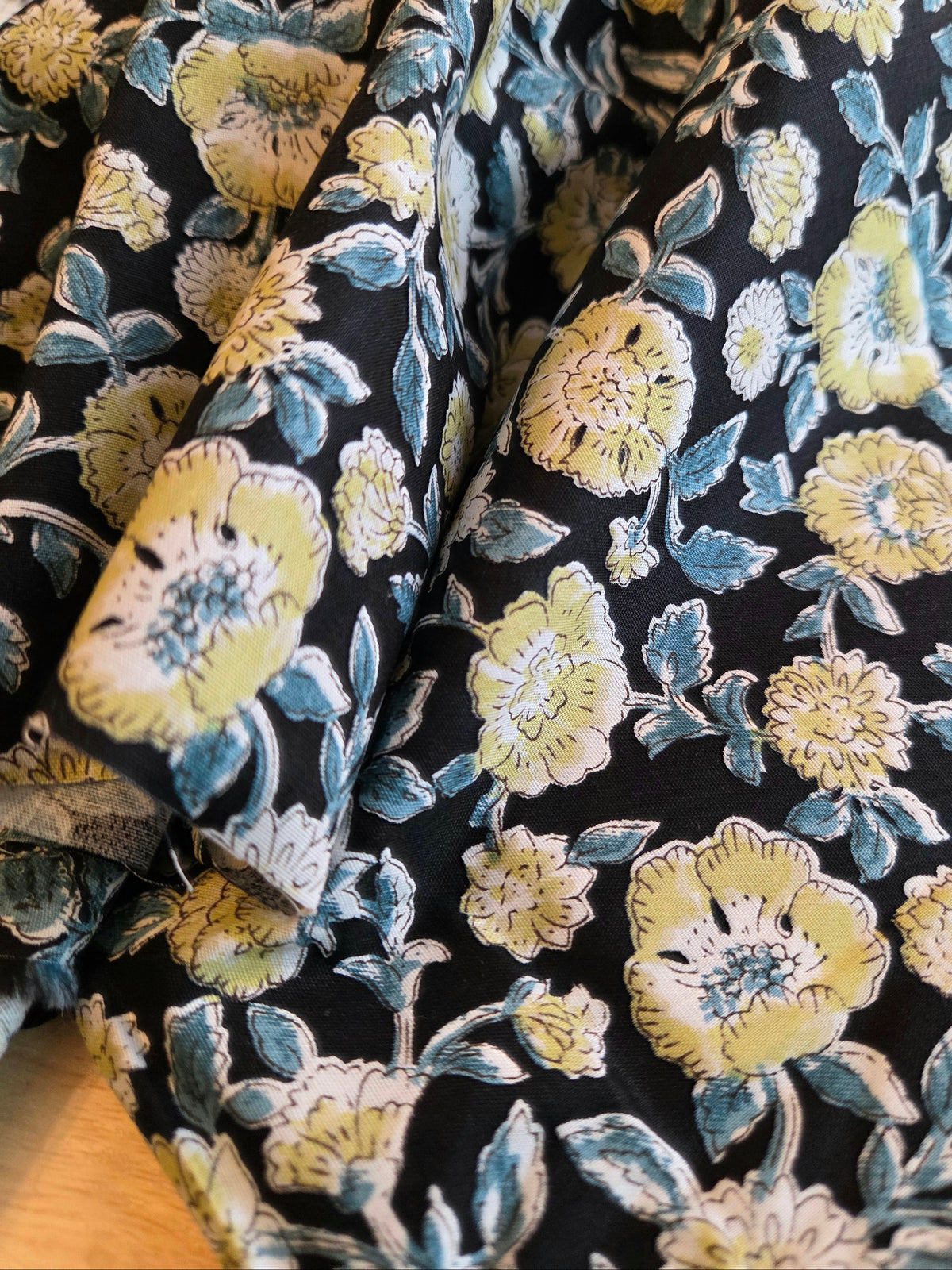 A close-up of a draped fabric with a dark navy background and a floral print featuring yellow, cream, and light blue flowers with green leaves.