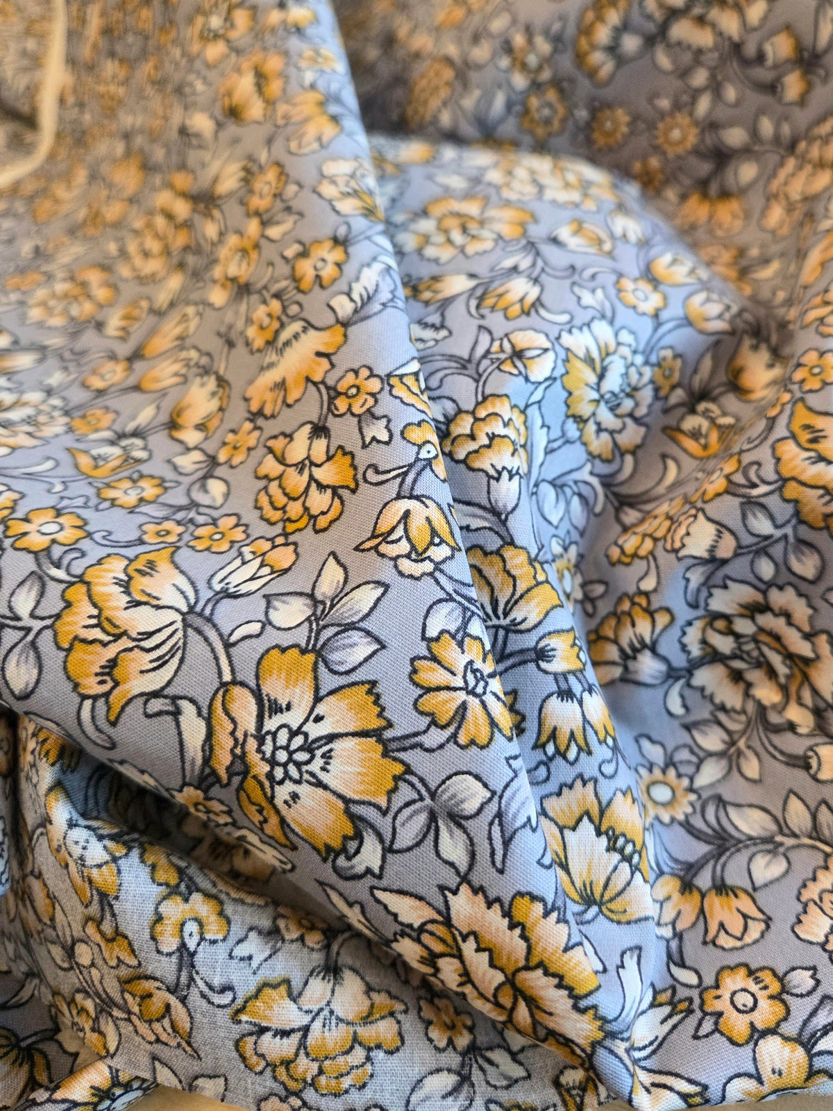 A close-up of draped floral fabric with a dusty blue-gray background and yellow, mustard, and white flowers outlined in dark gray.