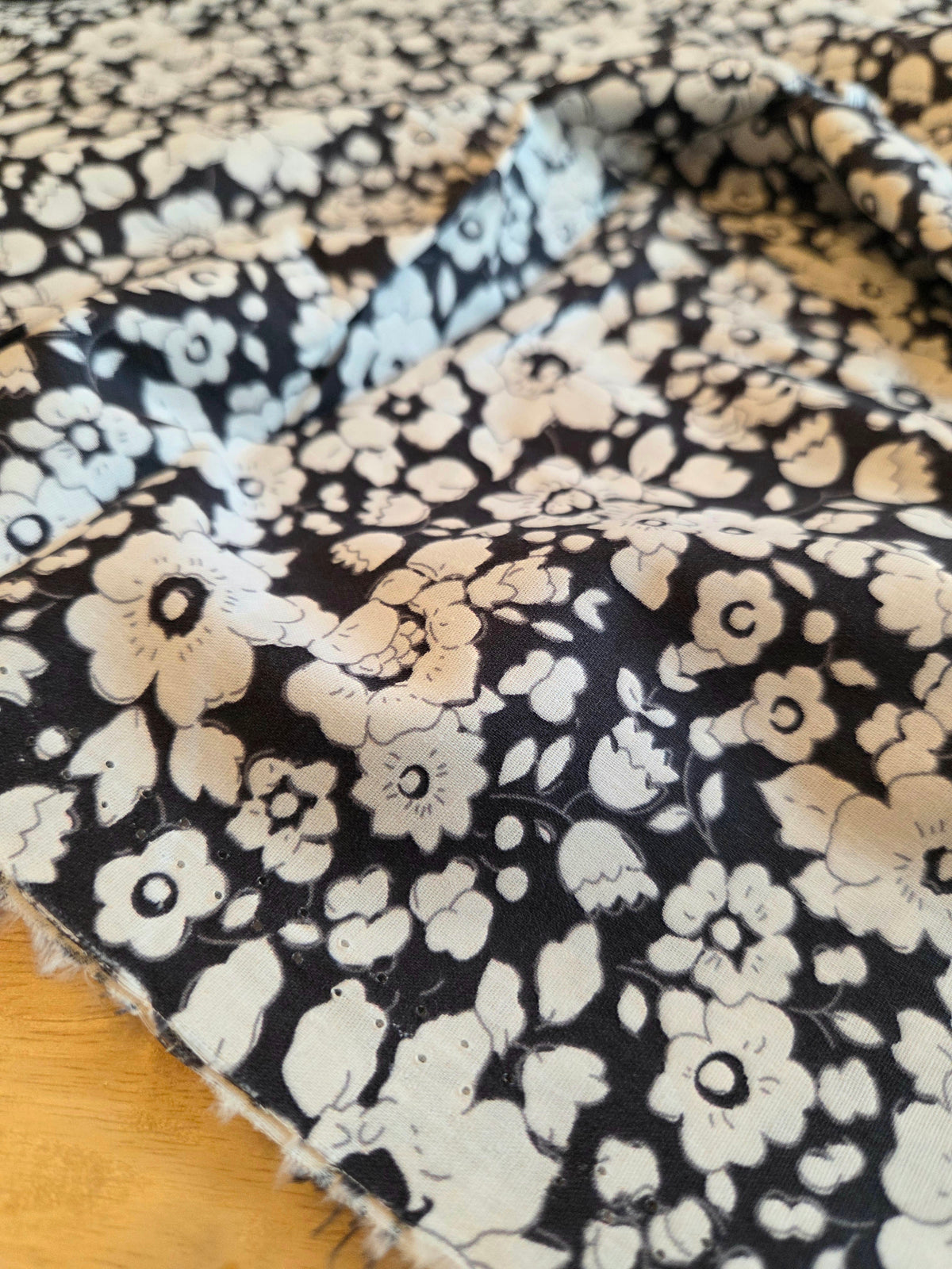 A close-up of a folded piece of fabric with a navy background and a dense white floral pattern, resting on a light wood surface.