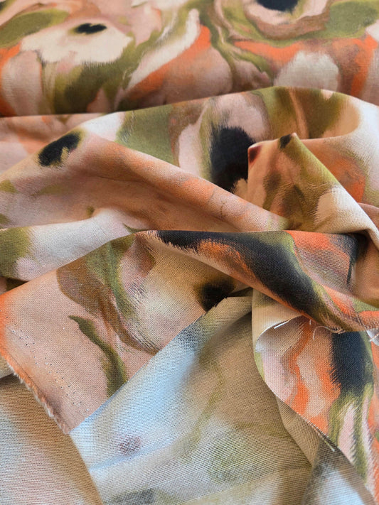 A close-up of draped fabric with an abstract floral or watercolor-style print in peach, orange, olive green, cream, and dark charcoal tones.