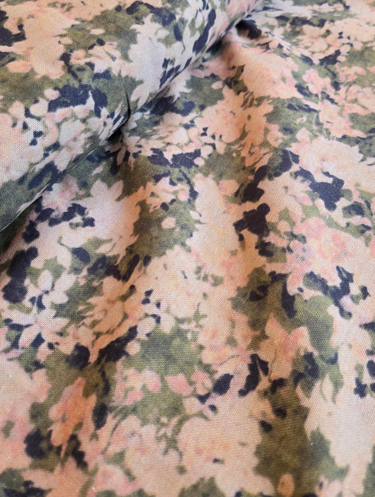 A close-up of draped fabric with an abstract floral or watercolor-like pattern in muted green, dusty pink, beige, and dark navy tones. LA FInch Fabrics