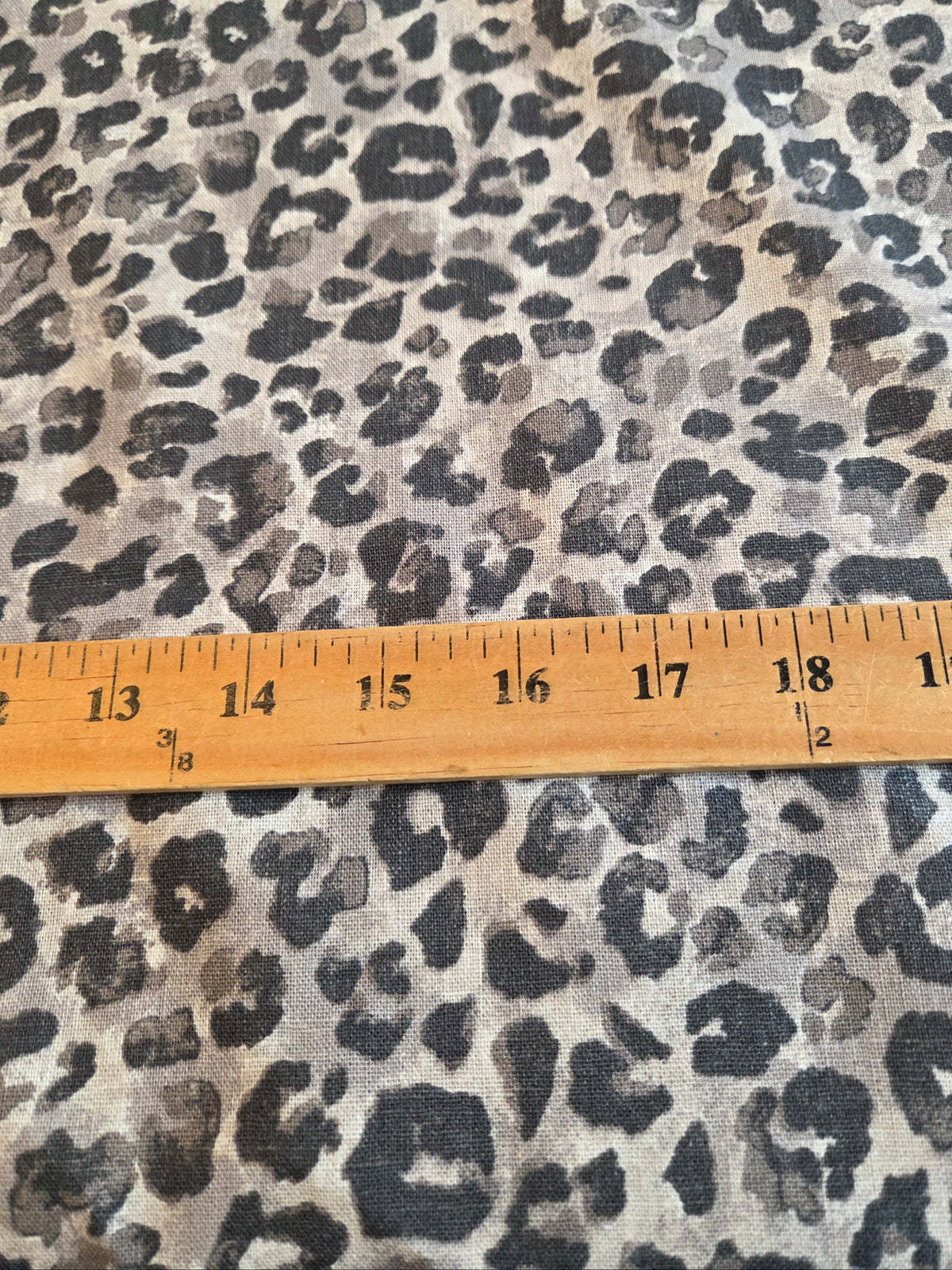 Leopard print fabric with a beige and gray base and black spots, shown with a wooden ruler for scale. LA Finch Fabrics by the yard fabrics available online and  in store