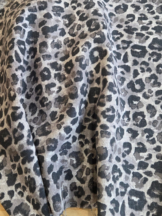 A piece of leopard print fabric draped over a wooden surface, showing a pattern of dark gray and black spots on a light gray base. LA Finch Fabrics
