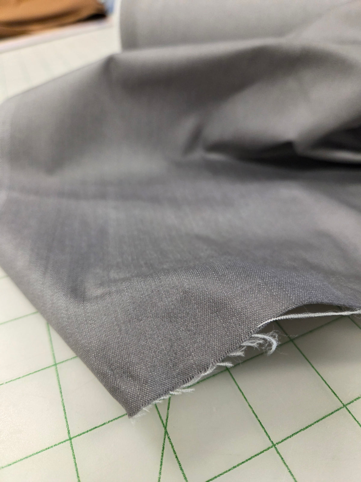 A close-up of folded gray fabric with a raw, frayed edge, resting on a white cutting mat with green grid lines.