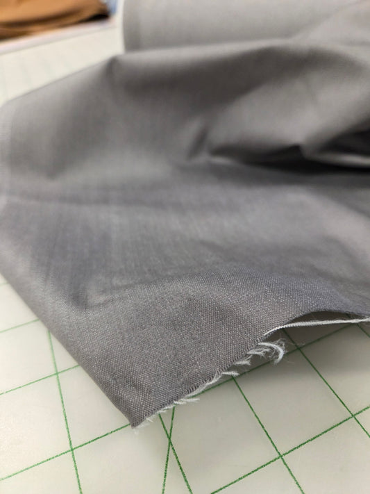 A close-up of folded gray fabric with a raw, frayed edge, resting on a white cutting mat with green grid lines.