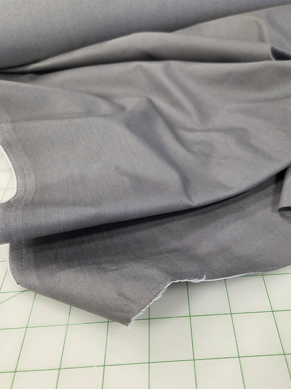 Gray fabric draped over a green-lined cutting mat.