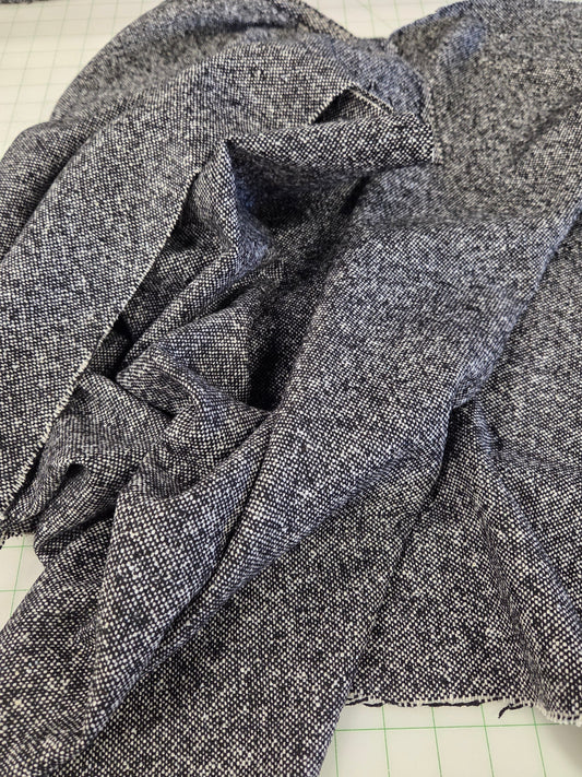 A close-up of dark heather gray fabric draped over a green grid cutting mat, with a matching folded piece of fabric visible along the top edge. italian wool blend tweed