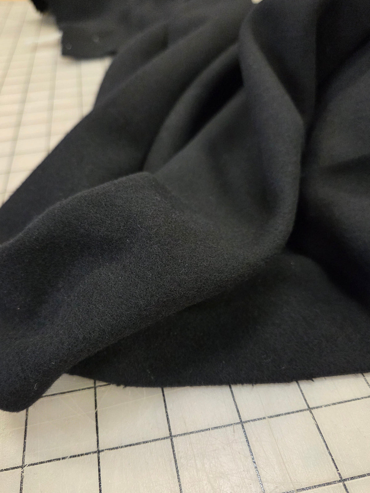 A close-up of draped black fabric with a soft, matte texture, laid over a white grid cutting mat.