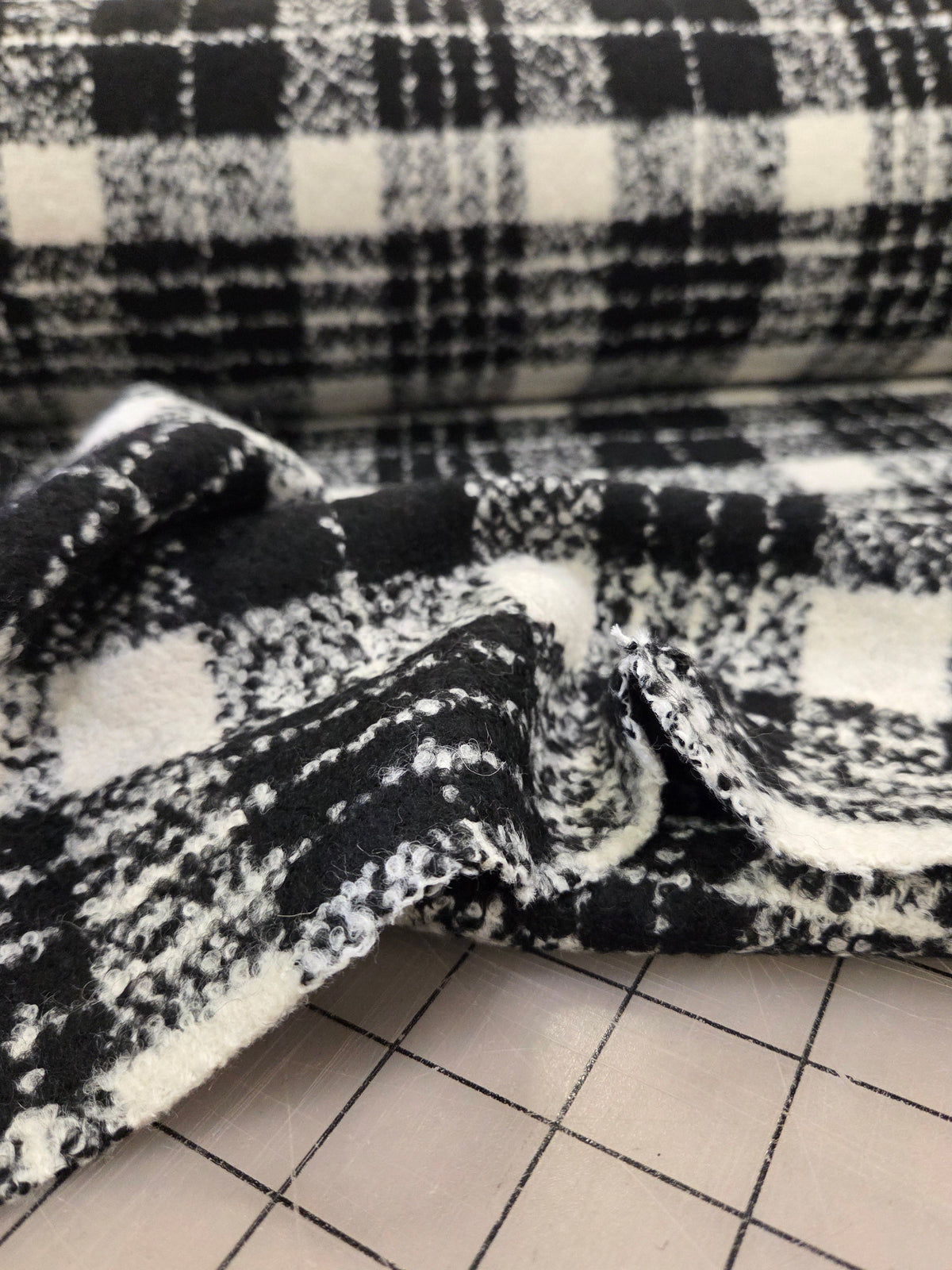 A close-up of a black and white plaid fabric, likely a blanket or throw, draped next to a white gridded surface.