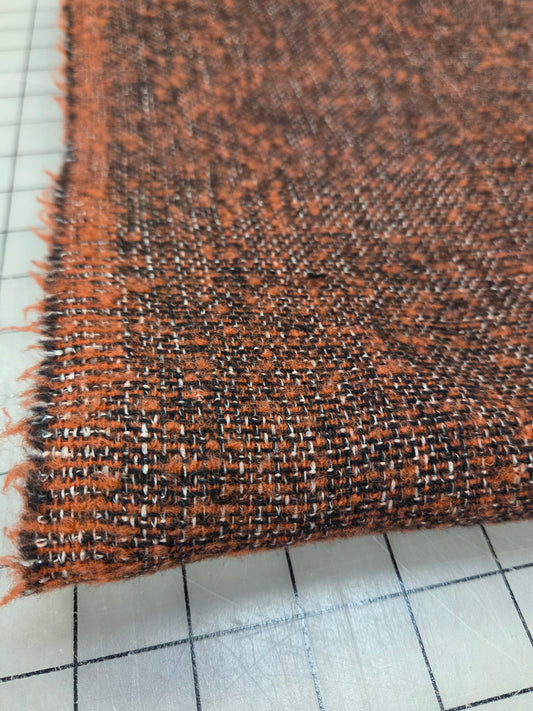 A close-up of a woven fabric swatch showing a textured blend of rust orange, black, and white threads, folded over on a white gridded cutting mat.