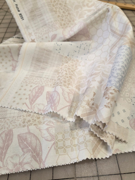 A folded stack of cotton fabric samples with various floral and geometric patterns in soft beige, dusty pink, and light blue, laid out on a gridded cutting mat.