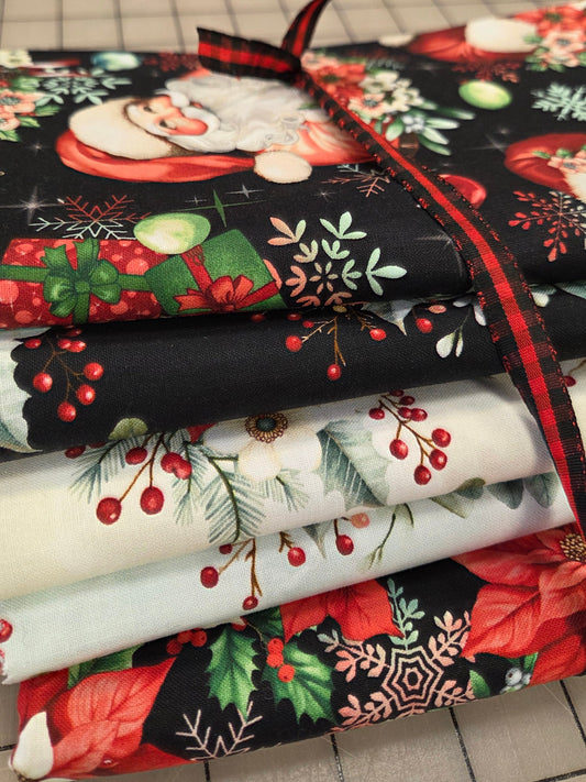 A stack of folded Christmas-themed fabric pieces tied with a red and black plaid ribbon, showing holiday prints including Santa, poinsettias, holly, berries, and snowflakes on a gridded cutting mat background.