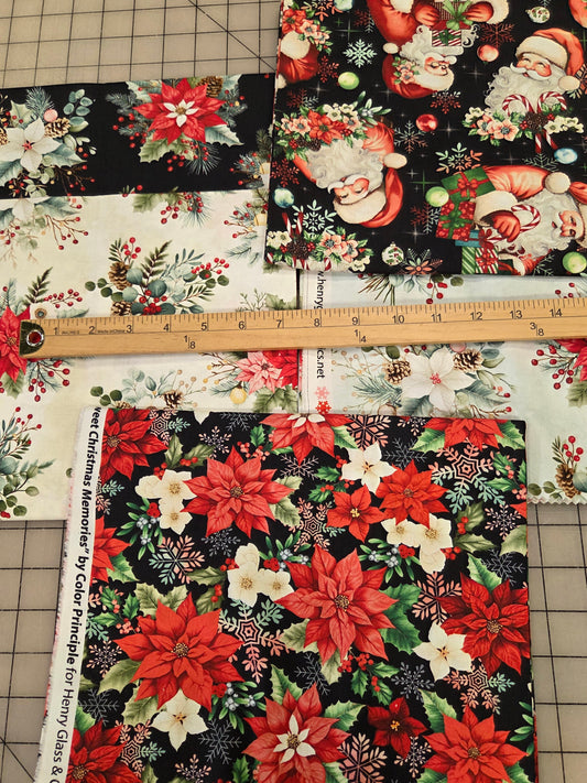 Three square fabric swatches with Christmas holiday prints are laid out on a gridded cutting mat with a wooden ruler in the center. The fabrics feature Santa Claus, poinsettias, and floral motifs in red, green, white, and black.