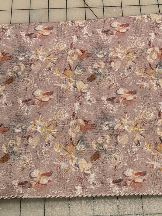 A square fabric swatch with a floral and butterfly pattern in muted pink, beige, and brown tones, displayed on a gridded cutting mat.