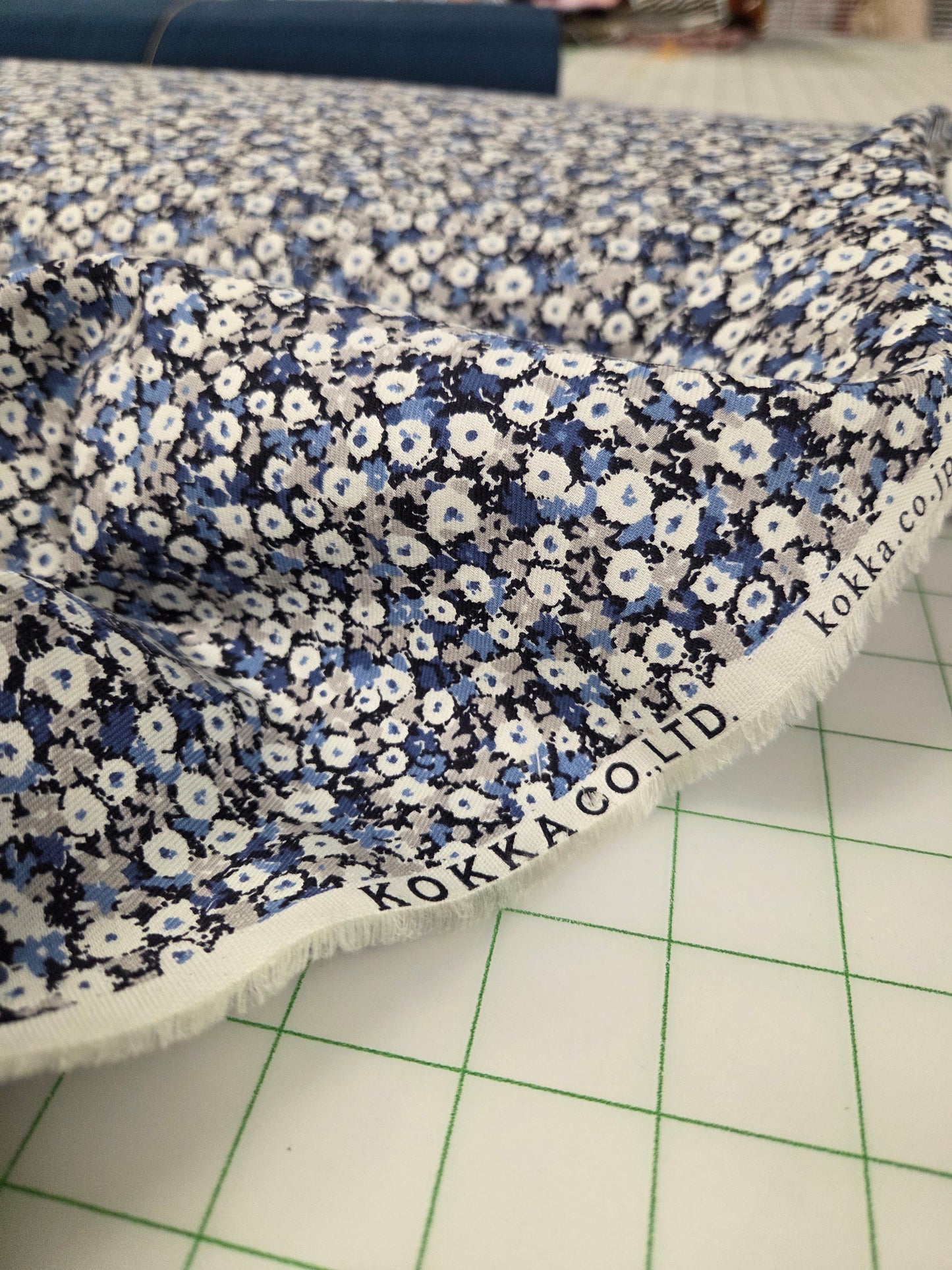 Floral fabric with blue and white pattern on a grid surface, featuring Koka Co. Ltd branding. Kokka ,Cotton