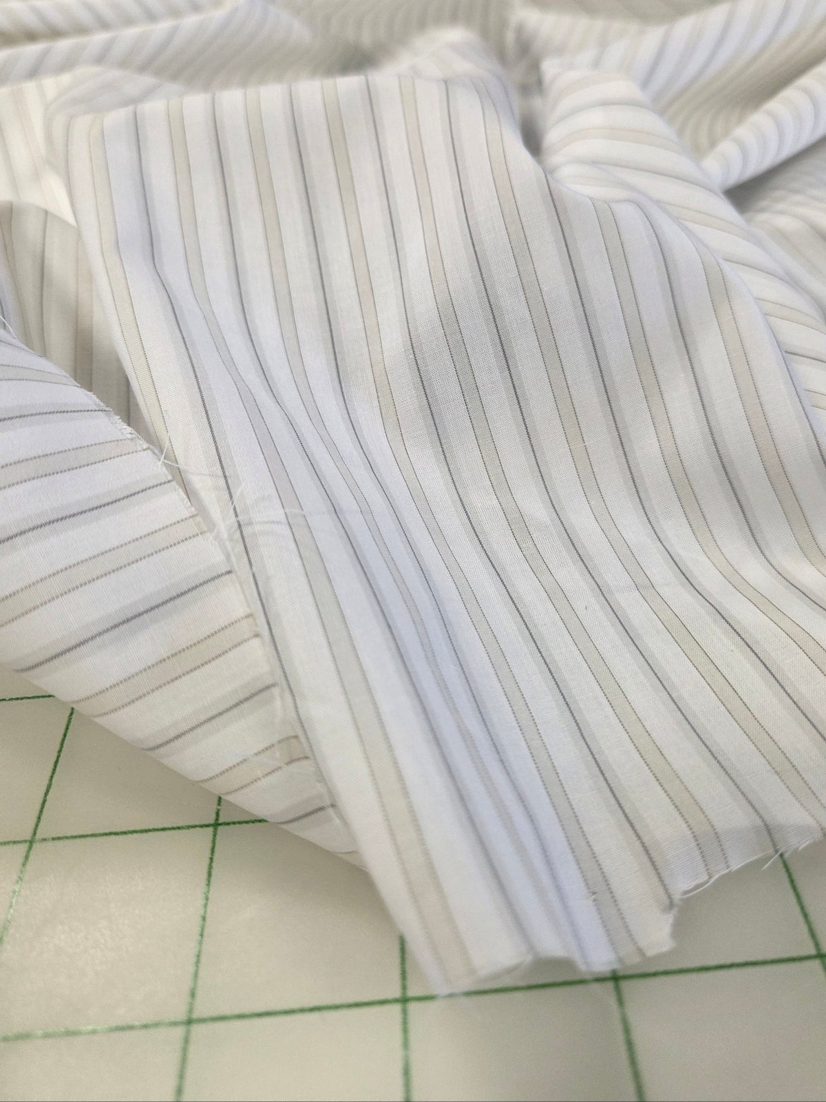 White pinstriped fabric with thin vertical gray stripes, draped on a green-lined cutting mat.