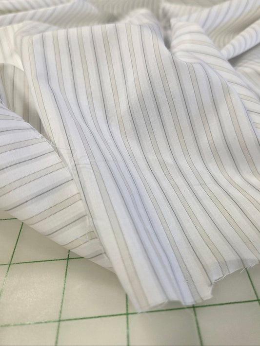 White pinstriped fabric with thin vertical gray stripes, draped on a green-lined cutting mat.