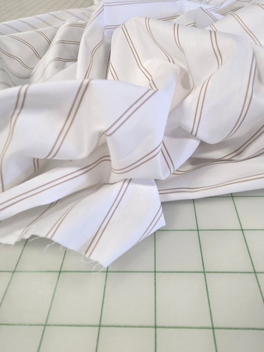 White fabric with thin tan stripes draped across a green-grid cutting table inside a sewing or fabric store.