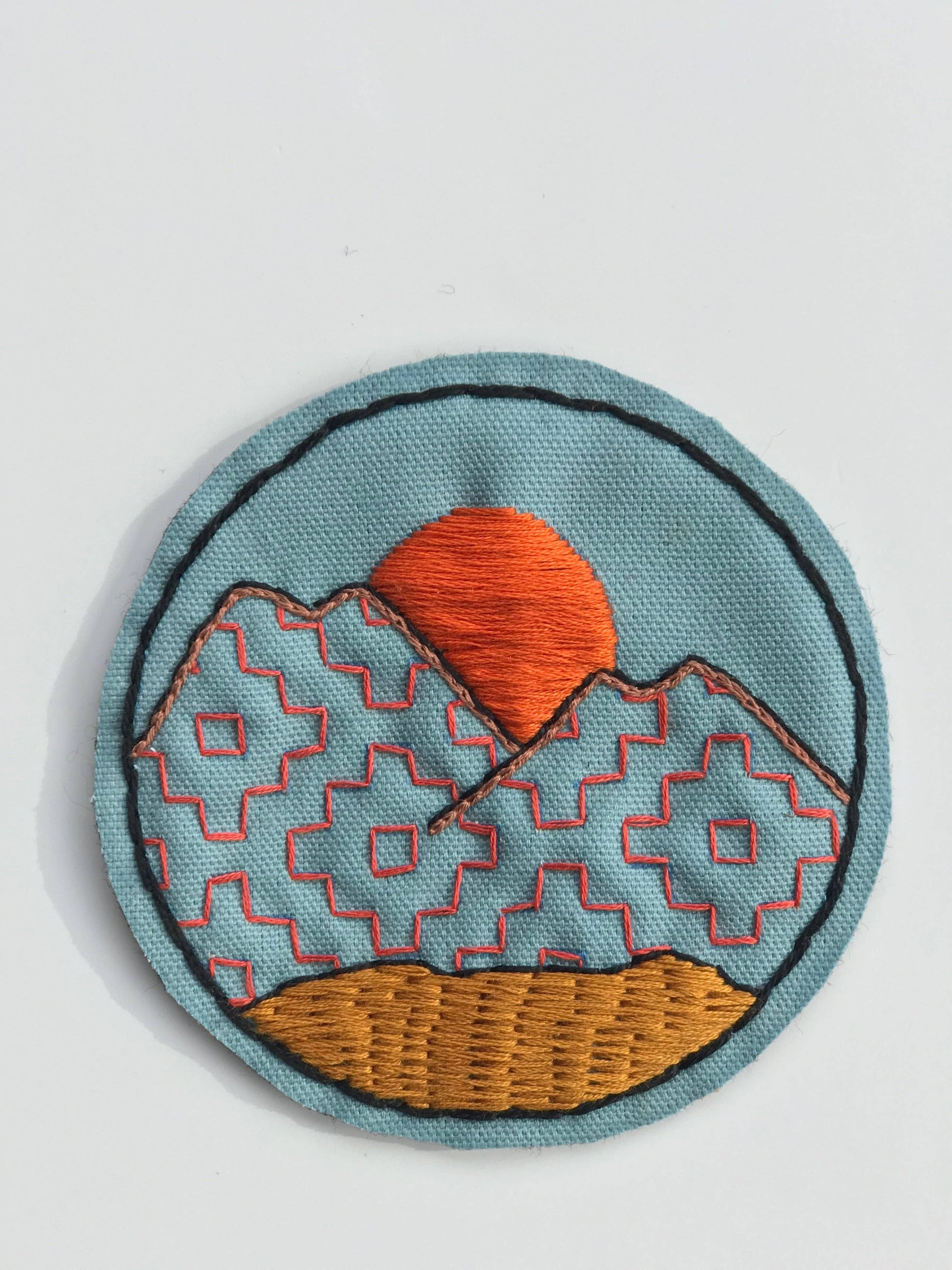 Embroidered patch with a sunset design on a light blue background