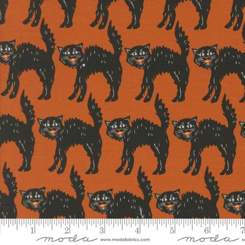 Pattern of black cats on orange fabric with a ruler for scale.