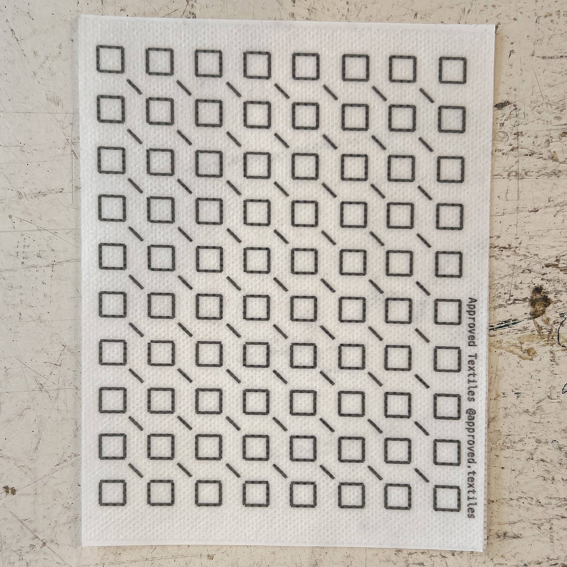 White cloth with black geometric pattern on a textured beige surface. mending supplies
