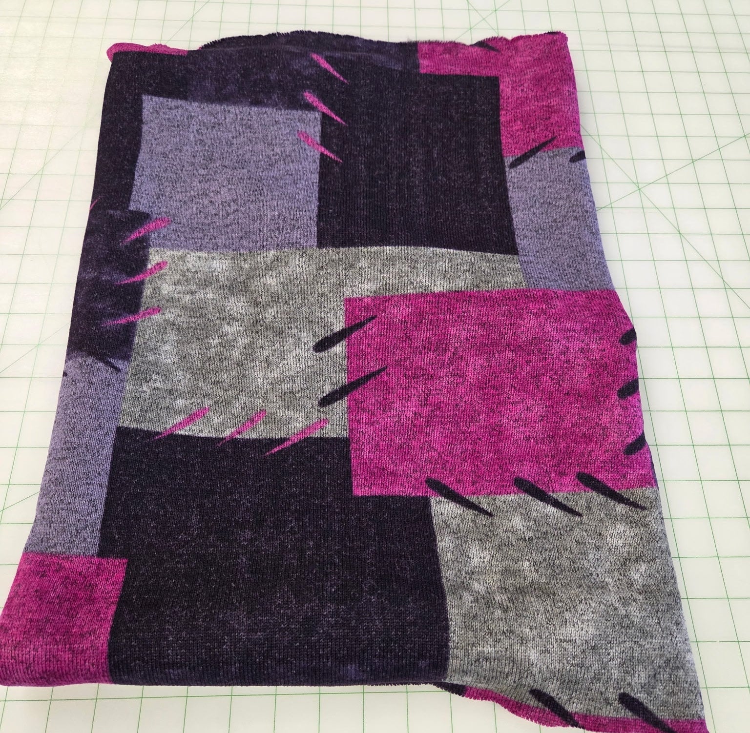 Patchwork fabric with purple, gray, and pink squares on a grid background. apparel hacci fleece for sewing garments. 