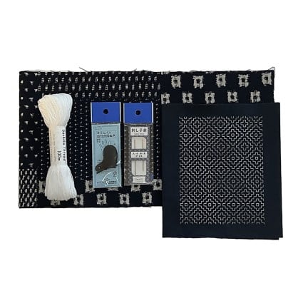 Black pouch with white patterns containing a white thread, blue labels, and a black sock on a white background.