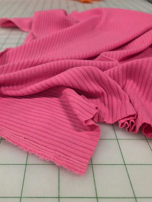 Pink fabric on a cutting mat with colorful fabrics in the background. Deadstock fabric. rib knit. poorboy rib. vibrant pink solid stretchy/