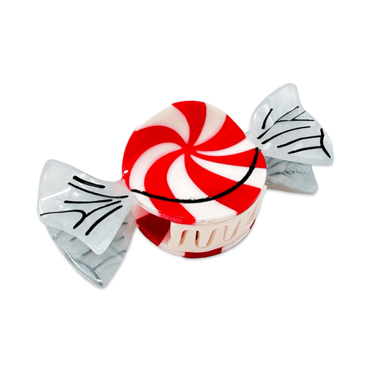 A novelty hair claw clip designed to look like a wrapped peppermint candy, featuring a red and white swirled top, a cream-colored wrapper, and clear wings with black line details on a white background.